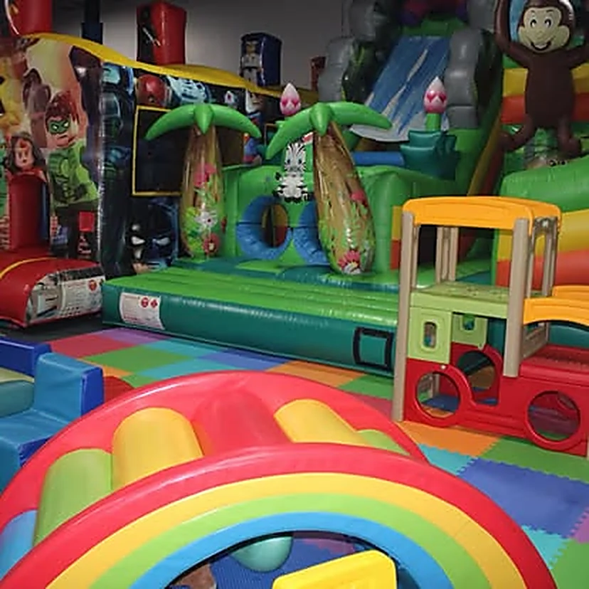 Playground de inflables con tema de jungla: palmeras, tobogán, mascota de mono y bloques de espuma de colores en el piso.