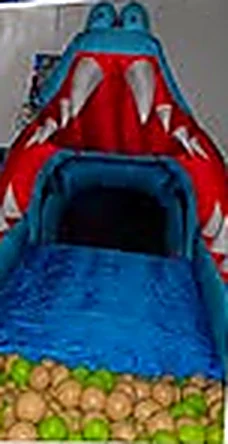 Tobogán inflable con forma de monstruo azul de boca roja que baja hasta una piscina de pelotas.